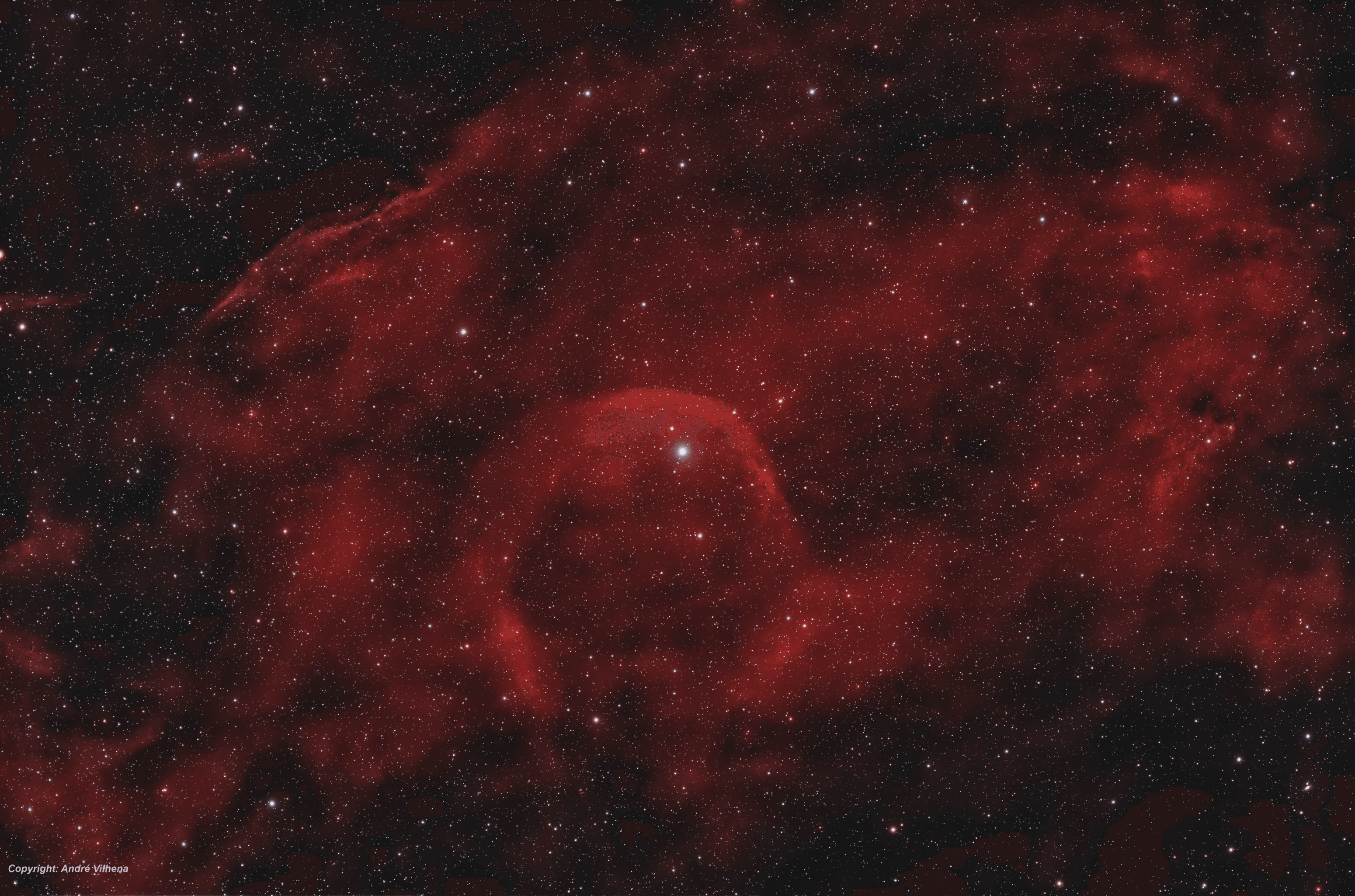 امتداد من الأغبرة الكونيّة التي تظهر بلون محمرّ يتوسّطها نجمٌ ساطع بارز، مع تناثر نجوم متفاوتة عبر الصورة