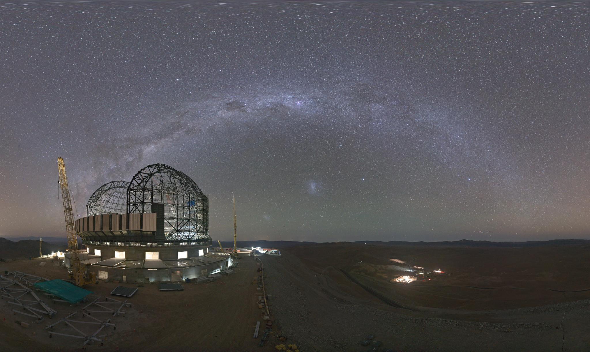 قوس درب التبّانة يمتدّ في سماء الليل بينما يظهر موقع بناء تلسكوب على يسار المقدّمة