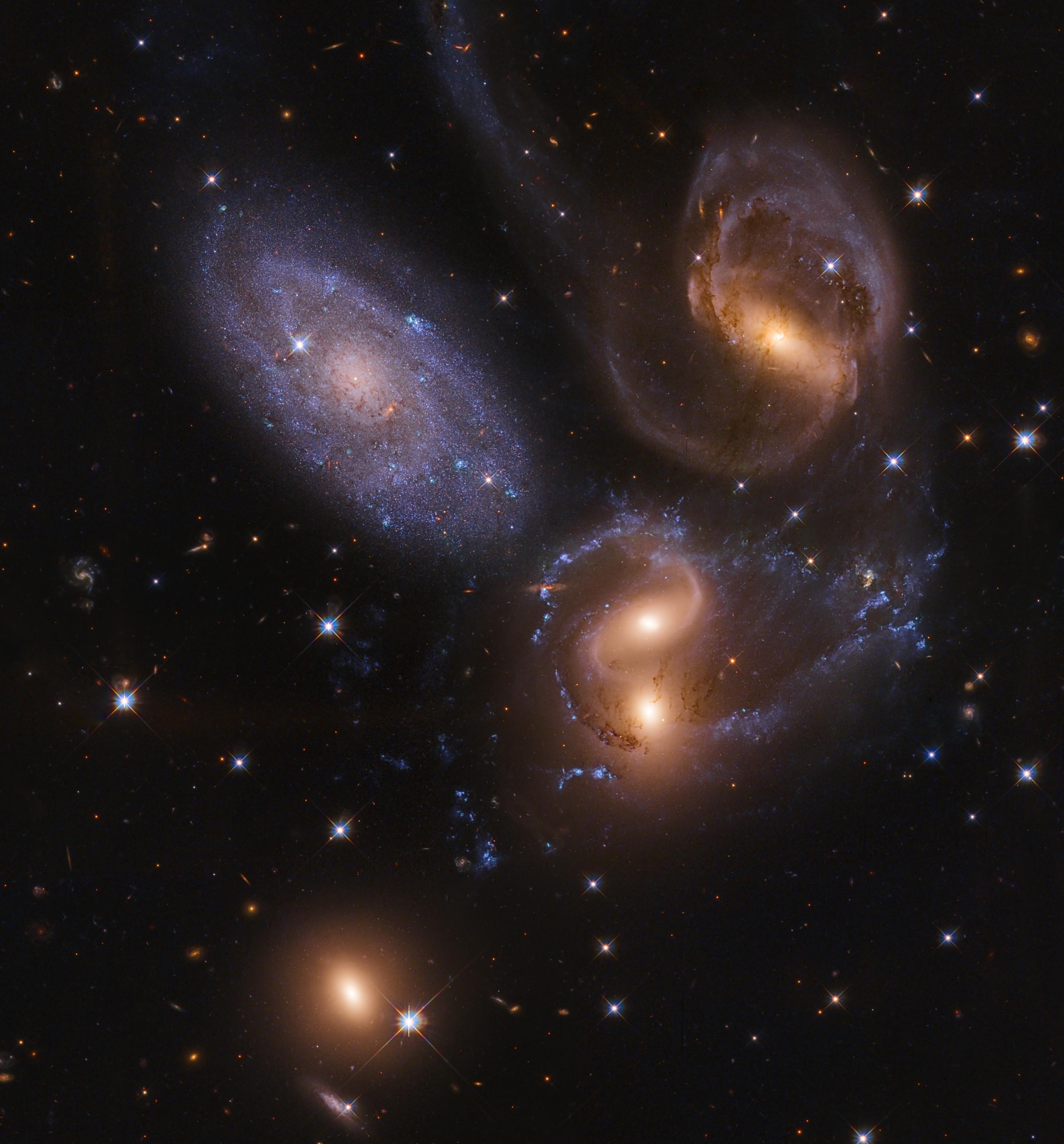 صورة أخّاذة للفضاء العميق تظهر عدداً من المجرّات بعضها ذو مسحة مصفرّة هي مجرّات بعيدة متفاعلة بينما هناك واحدة مزرقّة هي مجرّة أقرب. تتناثر نجوم المقدّمة المدبّبة على امتداد الصورة