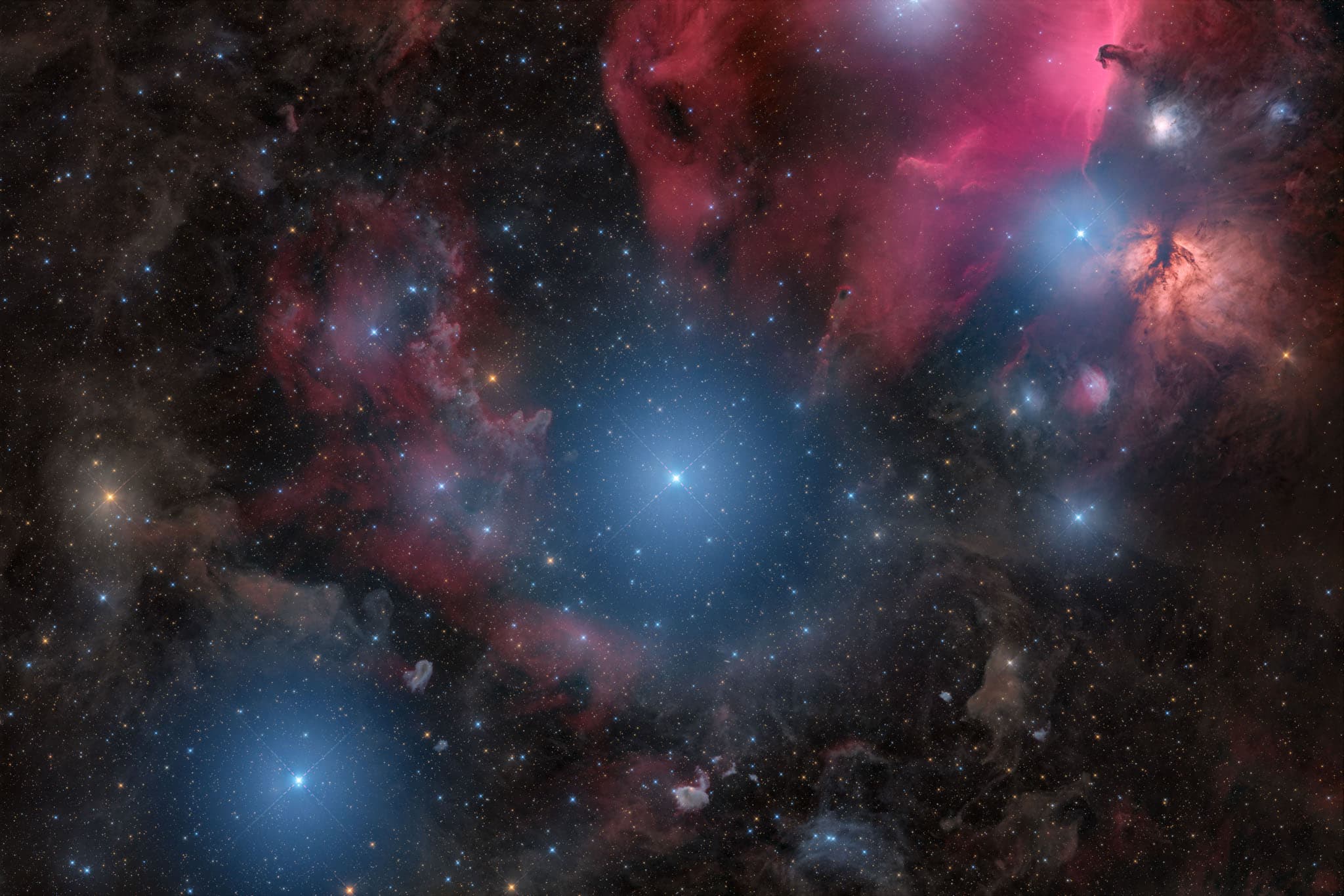 ثلاثة نجومٍ ساطعة مزرقّة تمتدّ بشكل قطري تنتشر حولها سدم بألوانٍ محمرّة في رقعة مرصّعة بالنجوم