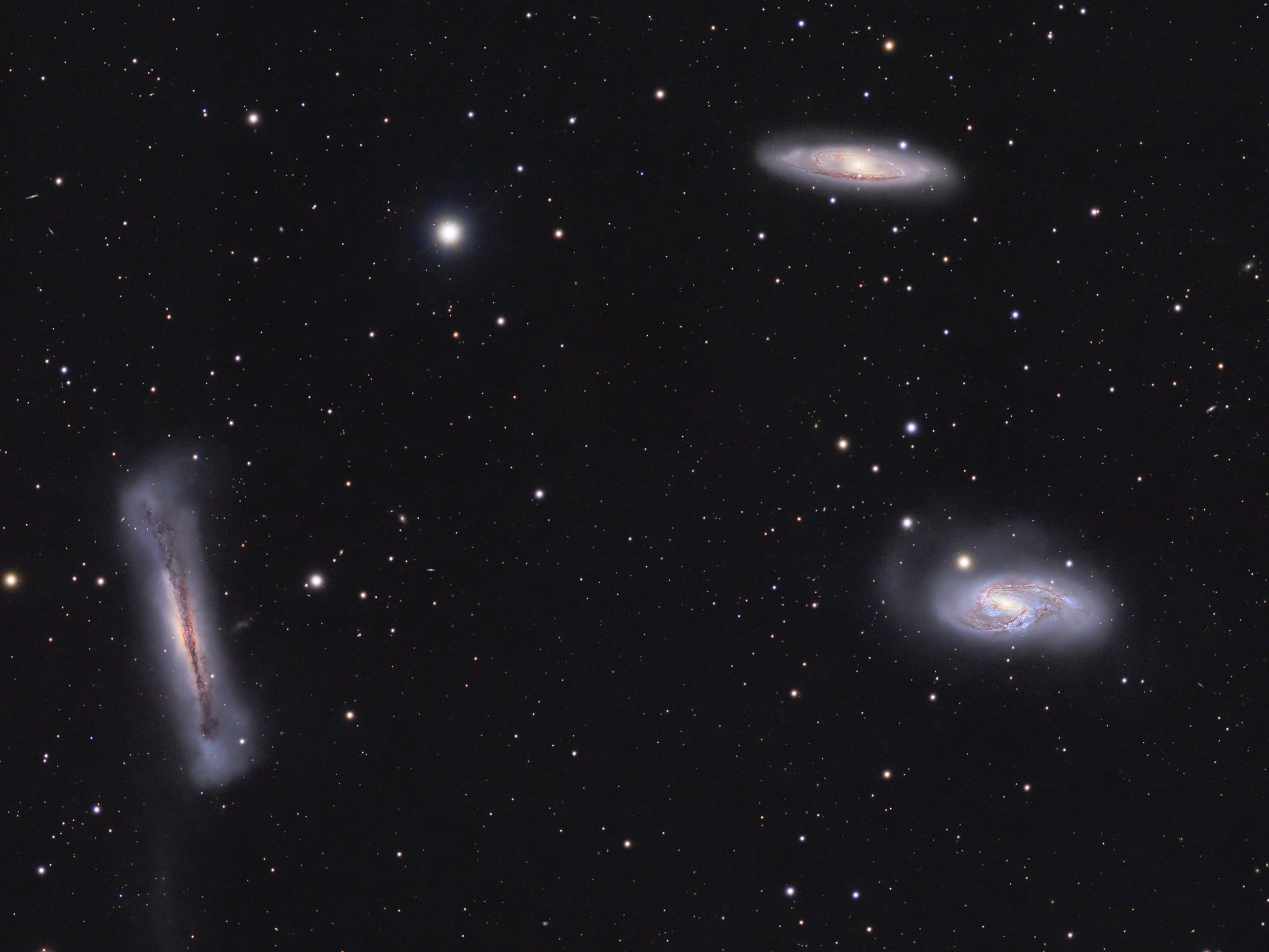 ثلاث مجرّات تُرى من زوايا مختلفة مع تناثر نجوم الخلفيّة عبر الصورة