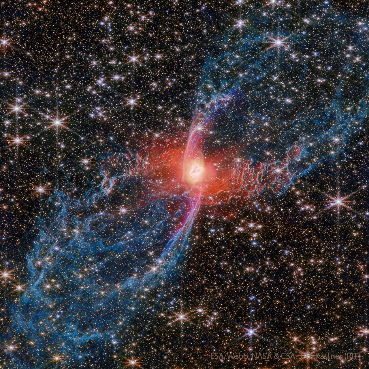 يُحيط حقلٌ نجميٌّ كثيفٌ بسديمٍ أزرق وأحمر يمتدّ من أسفل اليسار إلى أعلى اليمين. الأجزاء الخارجيّة للسديم زرقاء وخيطيّة، بينما الجزء الداخليّ أحمر وساطع.